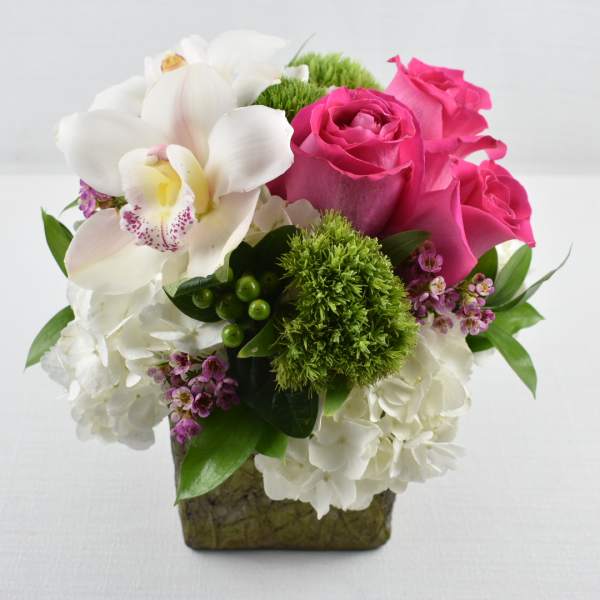 Compact arrangement of white hydrangeas, pink roses, and a white orchid in a green cube vase