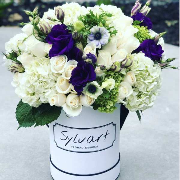 White and purple floral arrangement in a round hat box