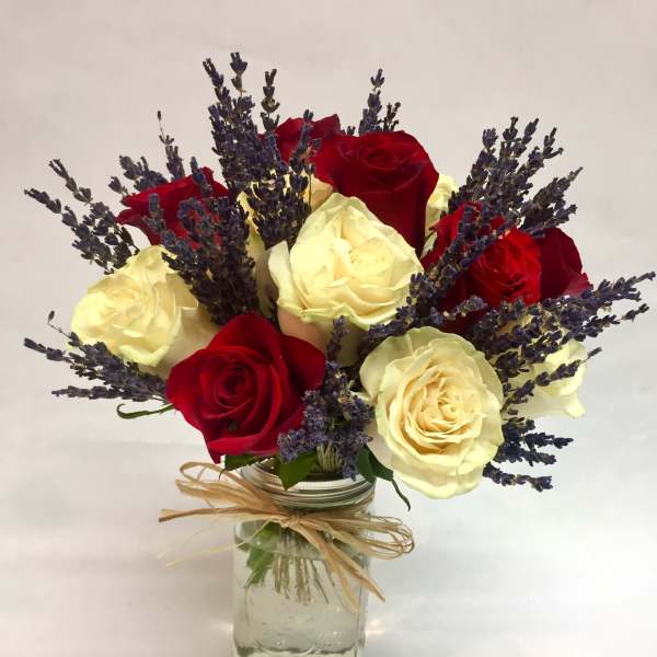 Red and cream roses with purple lavender in a glass jar vase