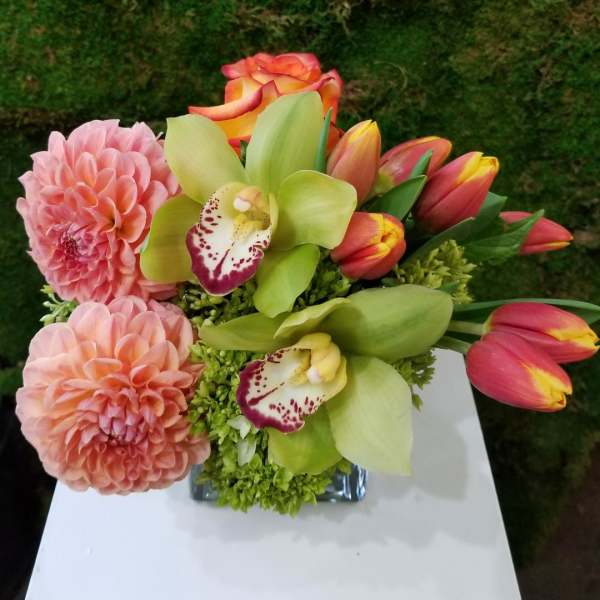Pink dahlias, green orchids, and tulips in a glass vase