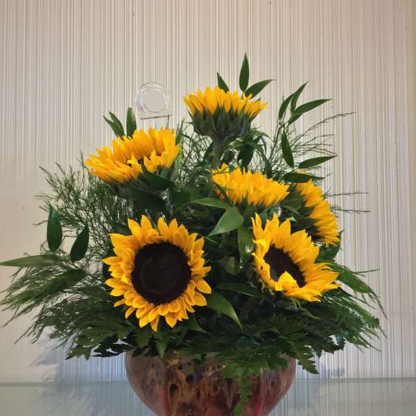 Sunflower arrangement in a glass bowl vase with dense greenery