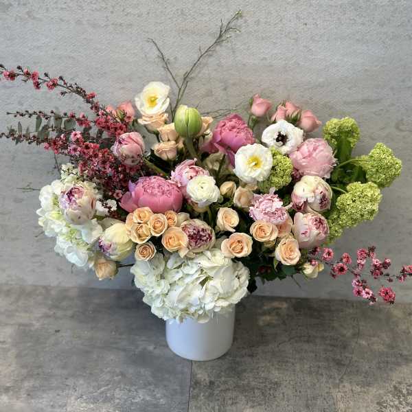 Large pastel flower arrangement in a white vase with pink, white, and peach blooms