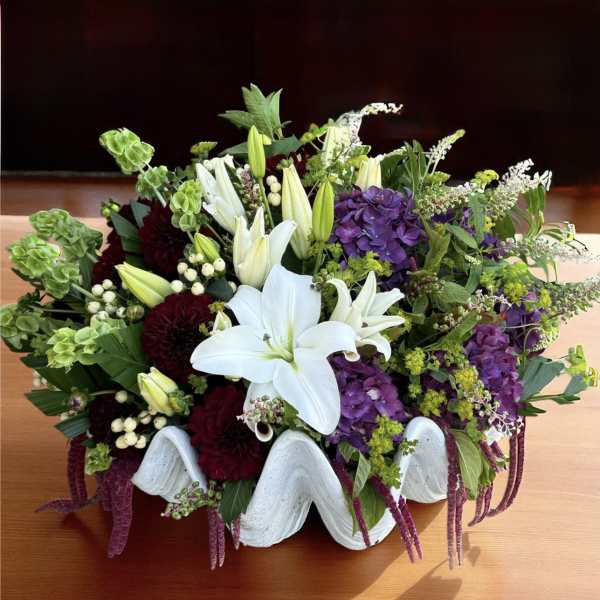 White lilies and purple flowers in a white shell-shaped container