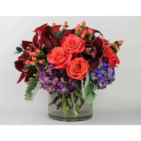 Bouquet of coral roses and purple flowers in a clear glass vase