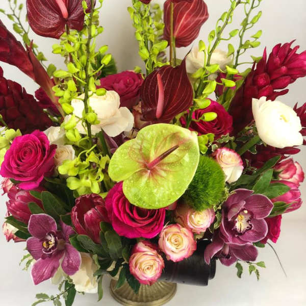 Tropical bouquet with burgundy anthuriums, roses, and orchids in a vase