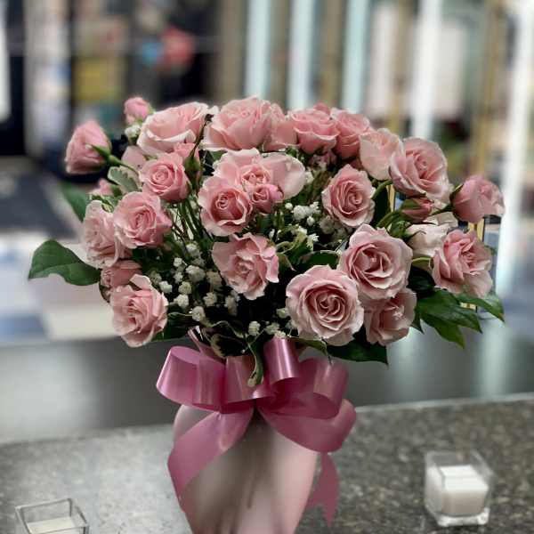 Pink roses arranged in a pink vase with a ribbon bow