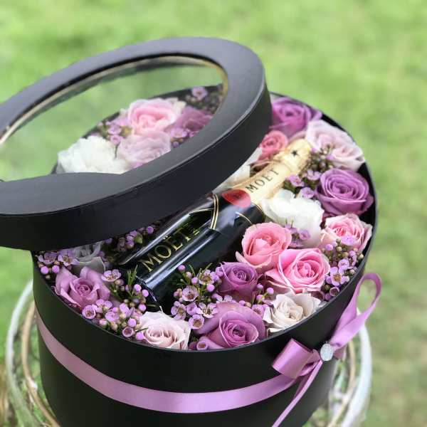 Round black gift box with pink and purple roses and a champagne bottle