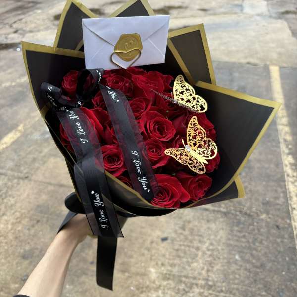 Bouquet of red roses wrapped in black and gold paper with ribbons and butterfly accents