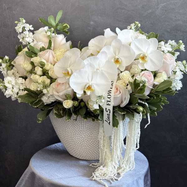White orchids and pale roses in a textured vase with trailing white strands