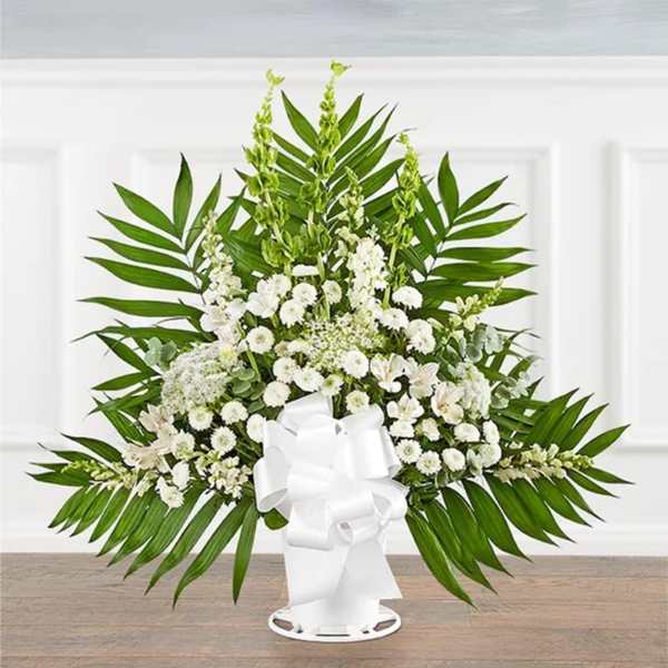 White floral standing spray with palm fronds and a white ribbon bow