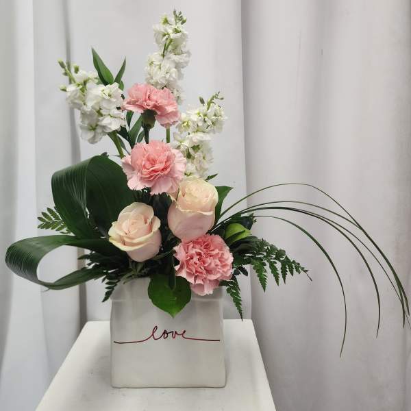 Pink roses and carnations with white blooms in a square vase