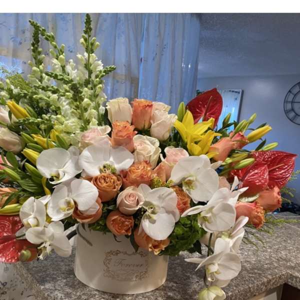 Mixed bouquet of white orchids, peach roses, yellow lilies, and red anthuriums in a white box