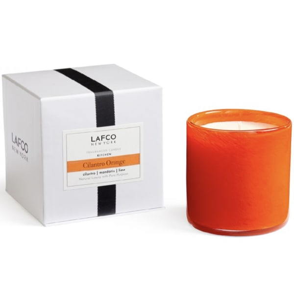 Orange candle in a glass jar beside a white gift box