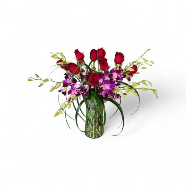 Red roses and purple orchids in a clear glass vase