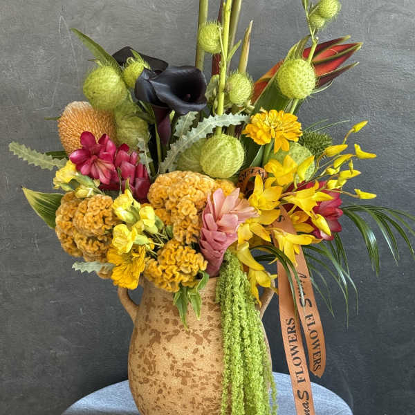 Mixed tropical bouquet in a speckled ceramic vase with bright yellow and pink blooms