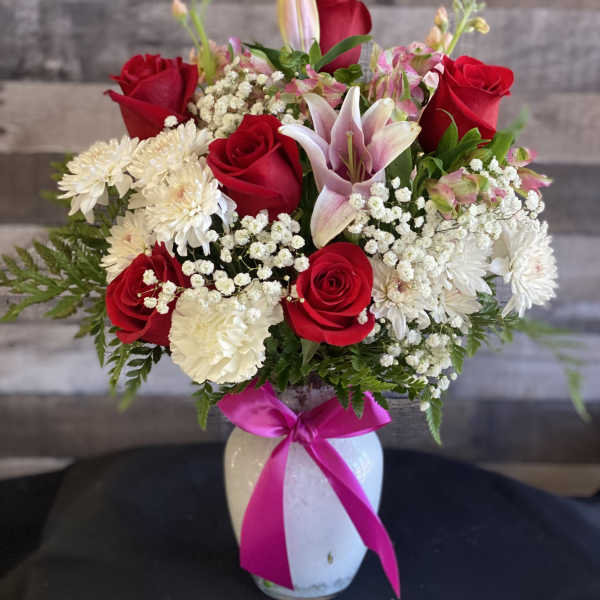 Bouquet of red roses, pink lilies, and white daisies in a white vase with a pink ribbon