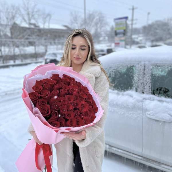 Woman holding a large bouquet of red roses wrapped in pink paper