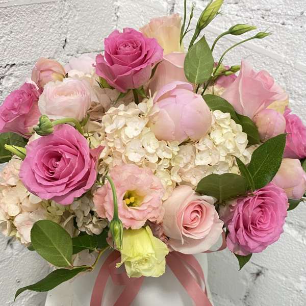 Pink roses and pale blooms arranged in a white vase with a ribbon
