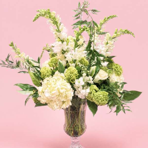 Cream and green floral arrangement in a clear pedestal vase