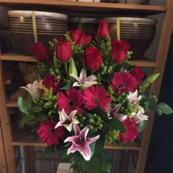 Bouquet of red roses, pink lilies, and magenta gerbera daisies in a glass vase