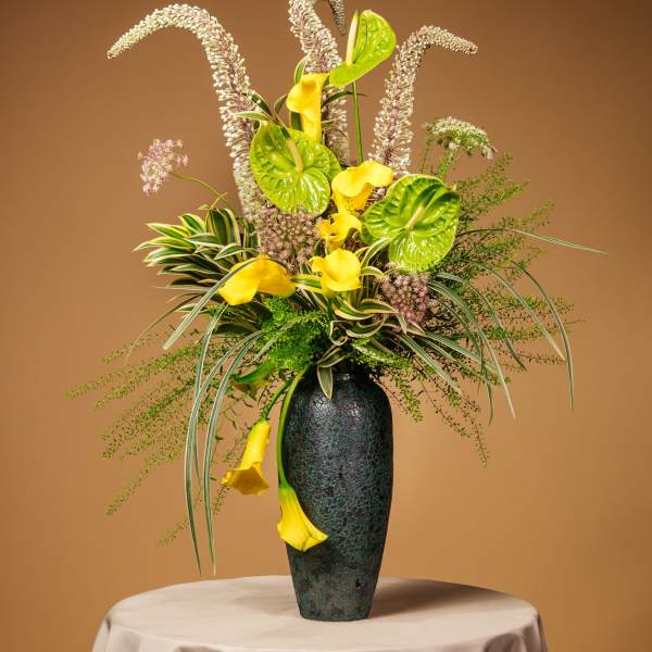 Tall floral arrangement with yellow calla lilies in a dark vase