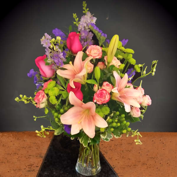 Mixed bouquet of pink lilies, roses, and purple flowers in a glass vase