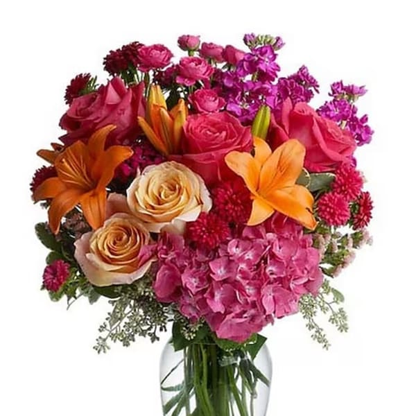 Mixed bouquet of roses, lilies, and pink blooms in a clear glass vase
