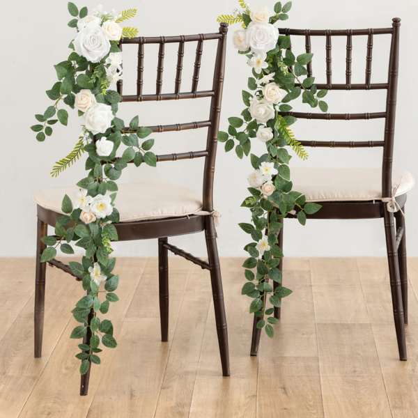 Pair of dark chairs decorated with cascading white and cream rose garlands with lush green foliage