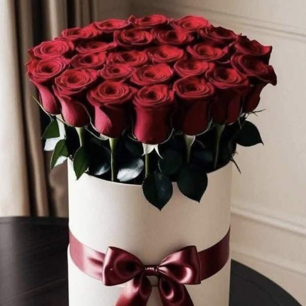 Red roses arranged in a white hat box with a burgundy ribbon