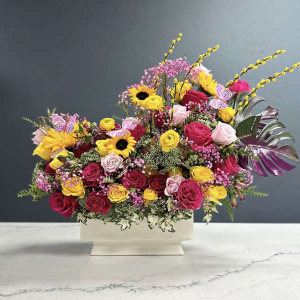 Mixed bouquet of pink, yellow, and red flowers in a white vase