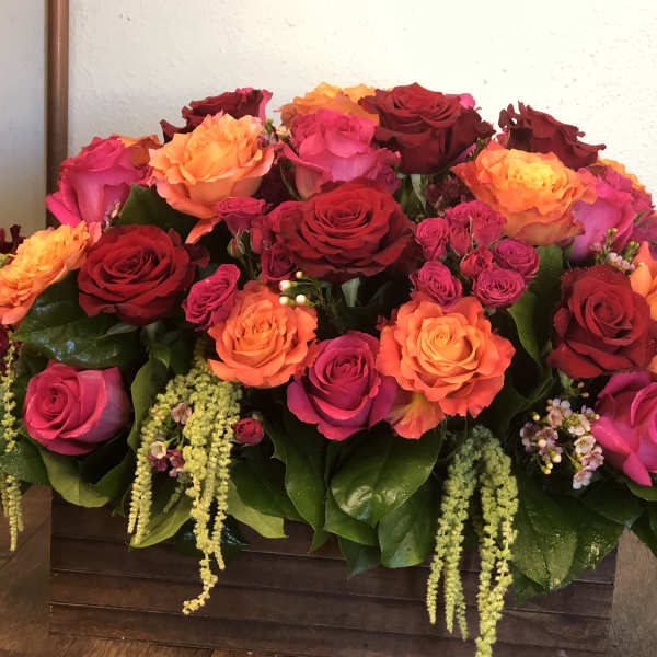 Low rectangular arrangement of red, orange, and hot pink roses in a wooden box