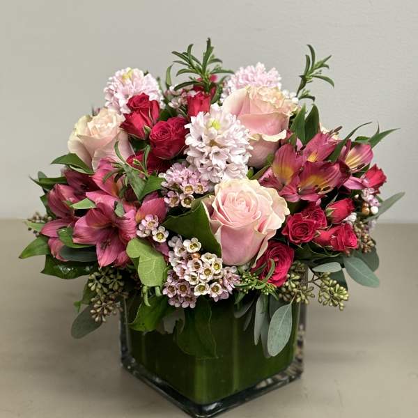 Compact arrangement of pink roses, hyacinths, and mixed blooms in a square glass vase