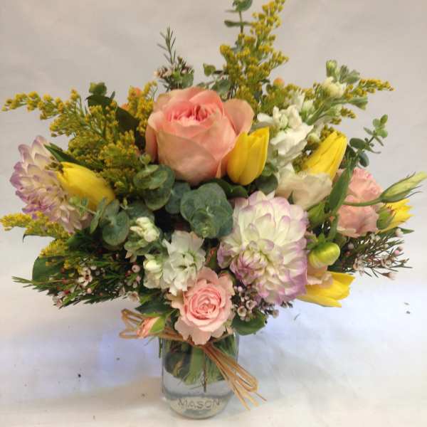 Pastel bouquet of pink roses, yellow tulips, and white blooms arranged in a mason jar vase.