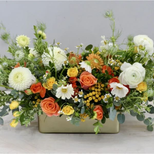 Low floral arrangement in a rectangular vase with white, orange, and yellow blooms
