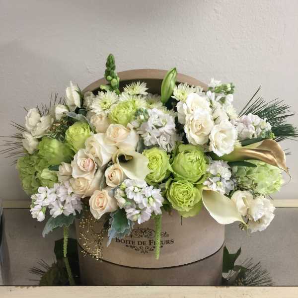 Green and white floral arrangement in a round box with roses and calla lilies