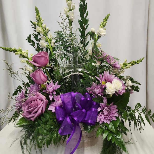 Purple and white floral arrangement in a clear cross vase with a purple ribbon