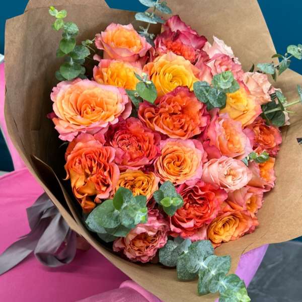 Bouquet of orange and pink roses wrapped in brown paper