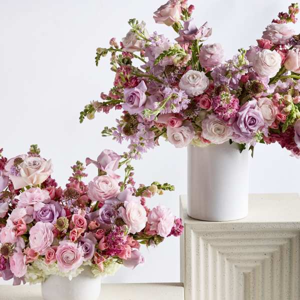 Two pink floral arrangements in white vases on textured pedestals