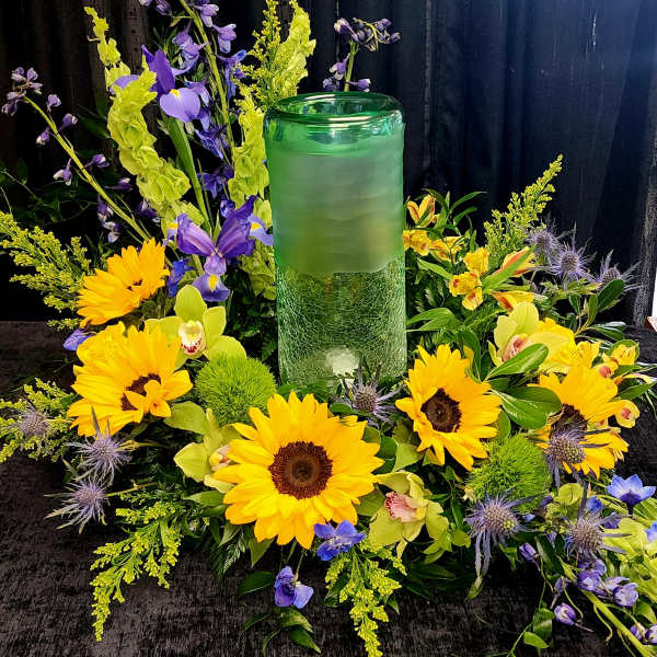 Yellow sunflowers and purple flowers arranged around a green glass candle holder