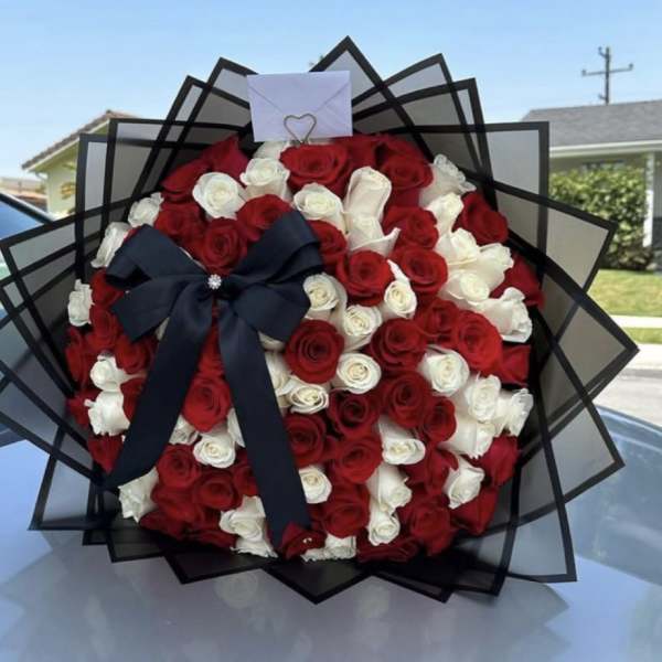Round bouquet of red and white roses with black wrap, black bow, and small envelope on top