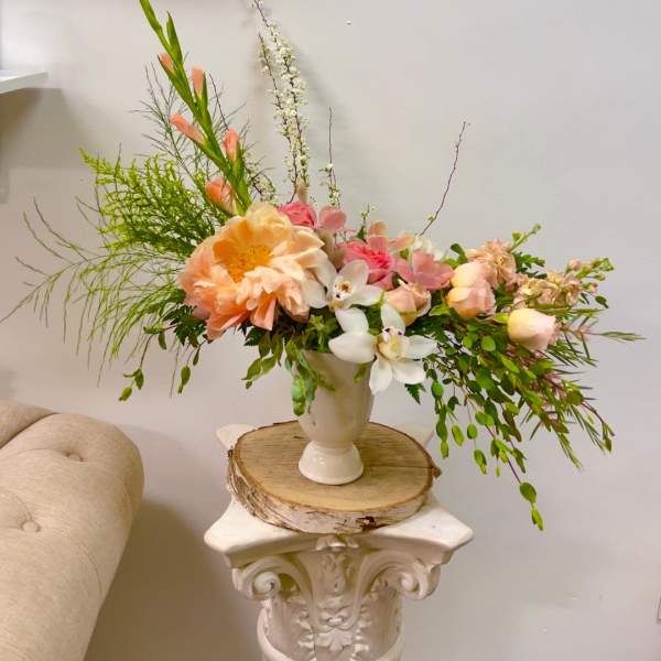 Peach and pink floral arrangement in a white vase on a pedestal