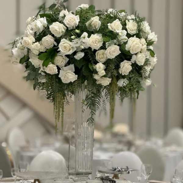 Tall white rose centerpiece in a clear glass vase on a banquet table