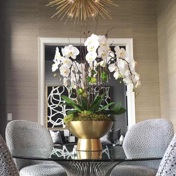 Tall white orchid arrangement in a gold bowl on a table