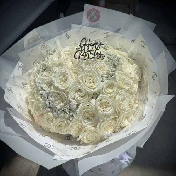 Bouquet of white roses wrapped in printed paper with a birthday topper