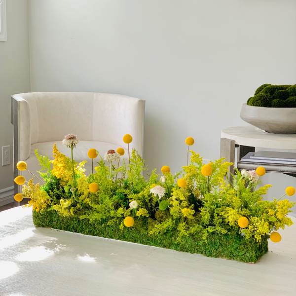 Low rectangular floral arrangement with yellow blooms on a table