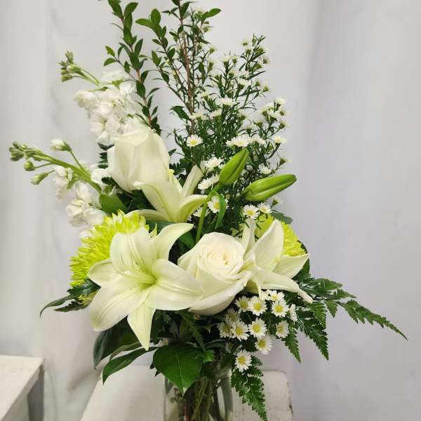 White lilies and roses in a glass vase with small white daisies