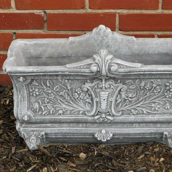 Ornate gray stone planter box against a brick wall