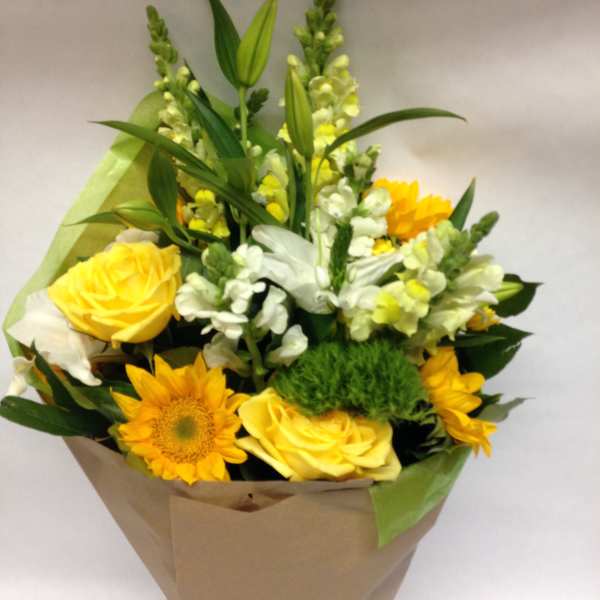Bouquet of yellow roses, sunflowers, and white snapdragons wrapped in paper