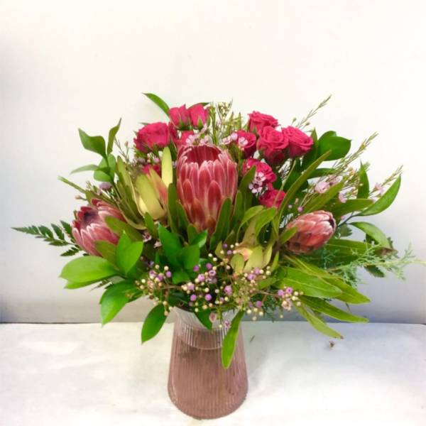 Pink protea and roses arranged in a ribbed glass vase