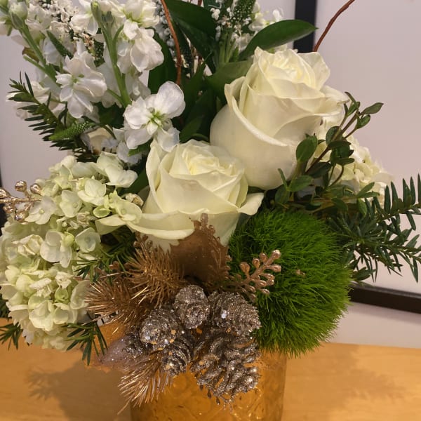 White roses and hydrangeas in a gold vase with silver pinecones